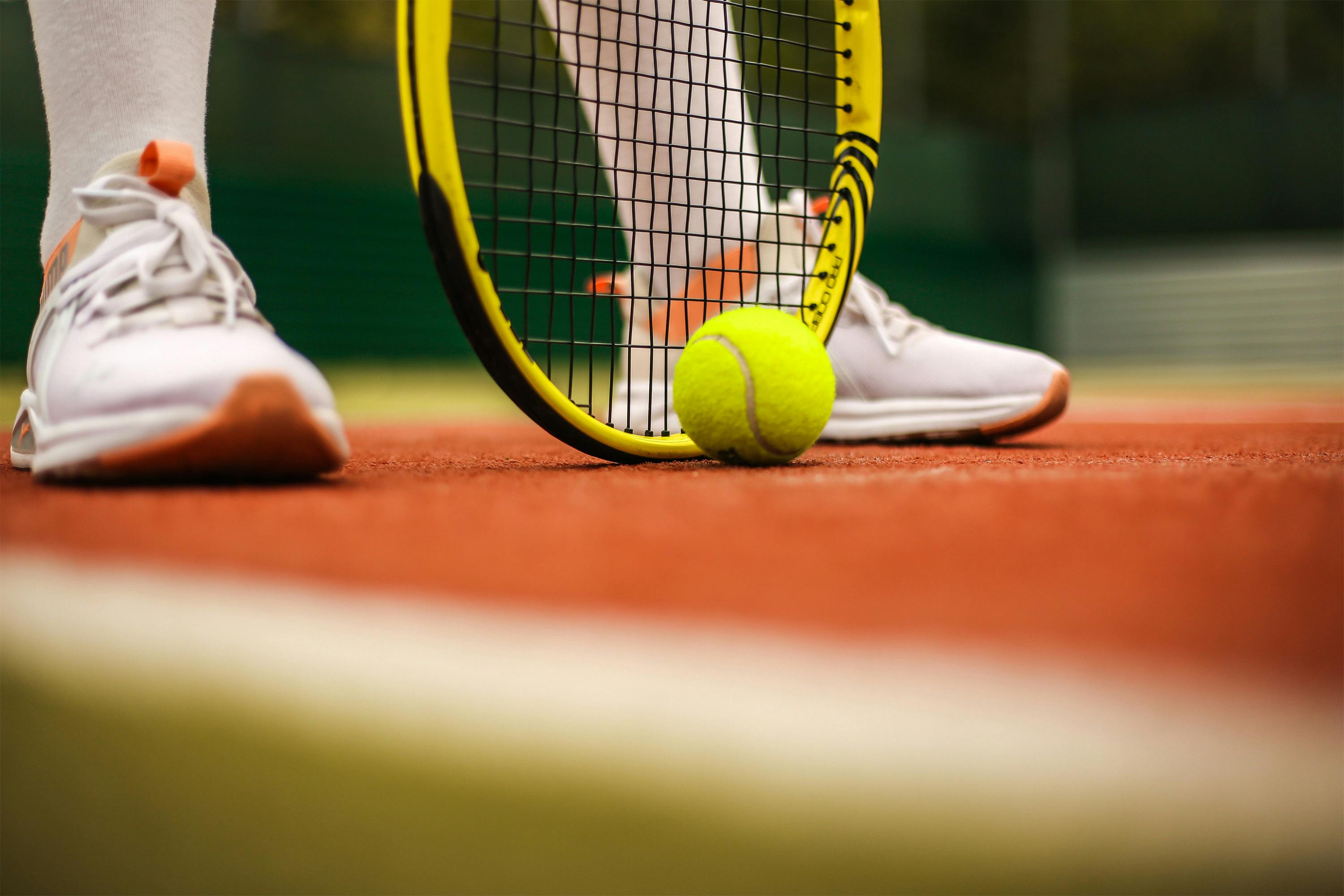 A tennis raquet being held down behind a tennis ball on a tennis court
